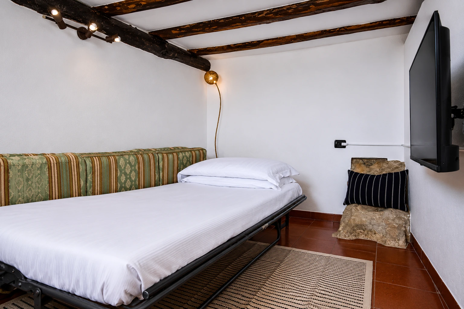Letto singolo nel soggiorno con travi a vista e televisore