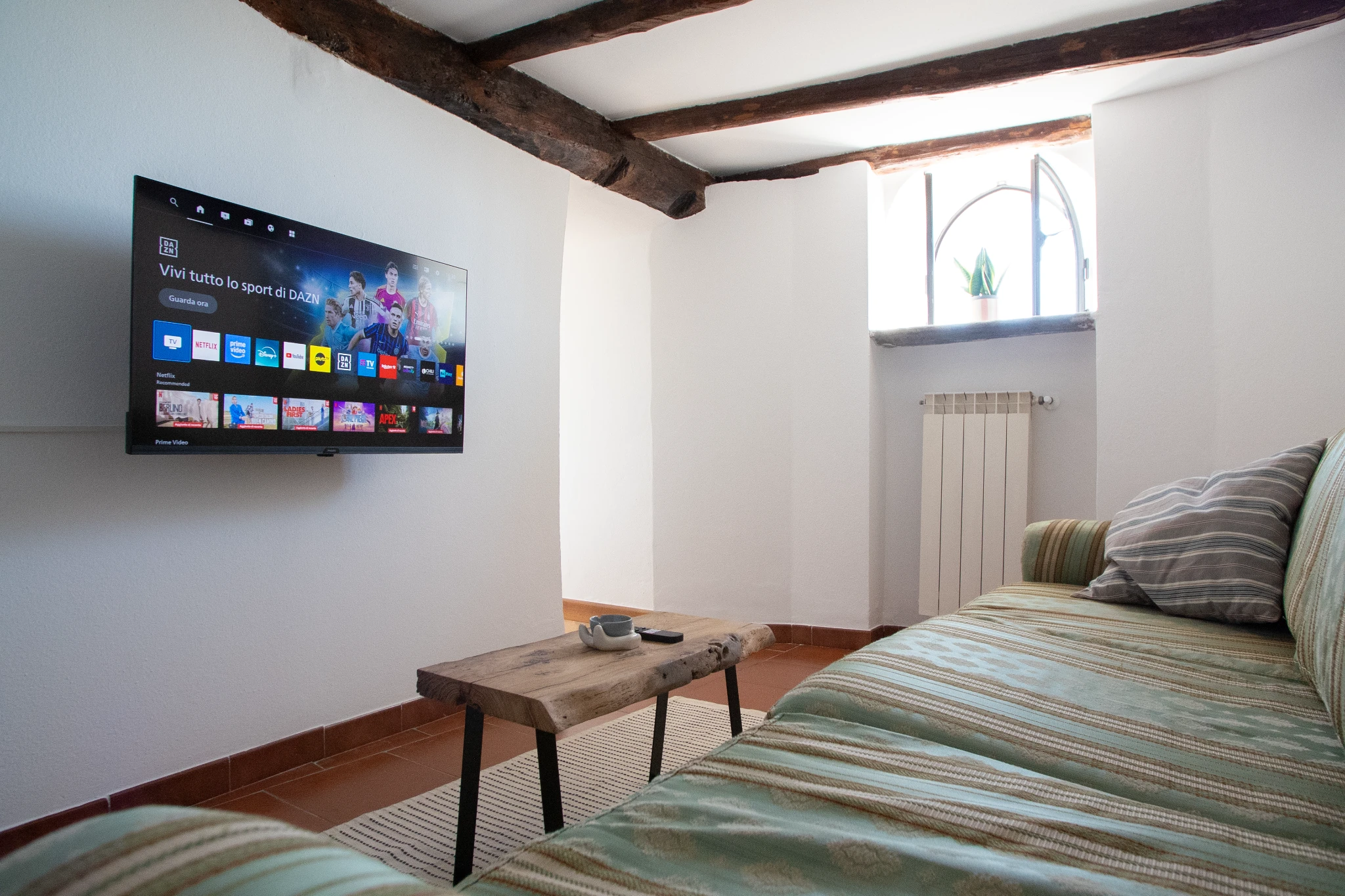 Soggiorno con divano, tavolino in legno, TV a parete e finestra ad arco
